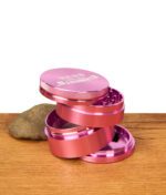 Zerlegter Elements Pink Grinder 4-teilig aus rosafarbenem Aluminium. Gestapelte Einzelteile zeigen den modularen Aufbau.