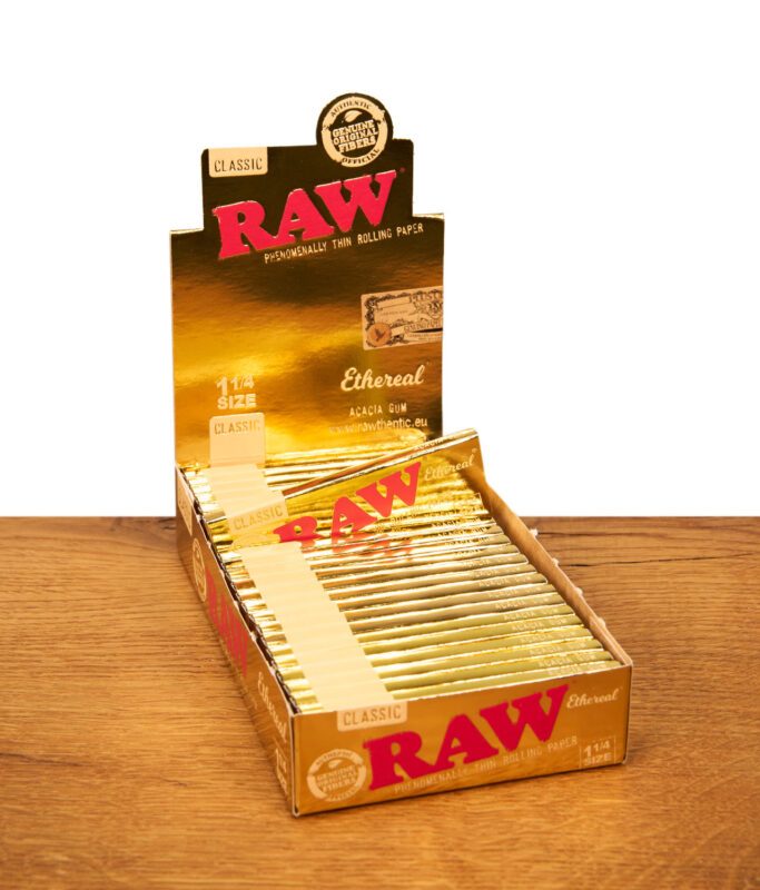 Zwei Packungen RAW Ethereal 1 1/4 Size Papers in glänzender Gold-Optik auf Holzoberfläche mit Naturstein-Akzent.