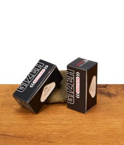 Zwei schwarze Gizeh Black Rolls Slim Packungen mit 5 Meter extra feinem Endlospapier auf einer Holzoberfläche vor einem Naturstein.