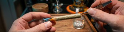 Glasfilter für Joints im Test: Ein handgedrehter Joint mit einem farbenfrohen Glas-Tip wird präsentiert, während das Ende präzise mit einer Pinzette bearbeitet wird.