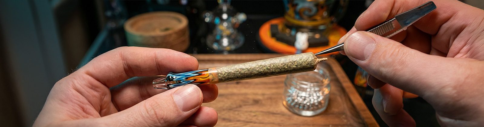 Glasfilter für Joints im Test: Ein handgedrehter Joint mit einem farbenfrohen Glas-Tip wird präsentiert, während das Ende präzise mit einer Pinzette bearbeitet wird.