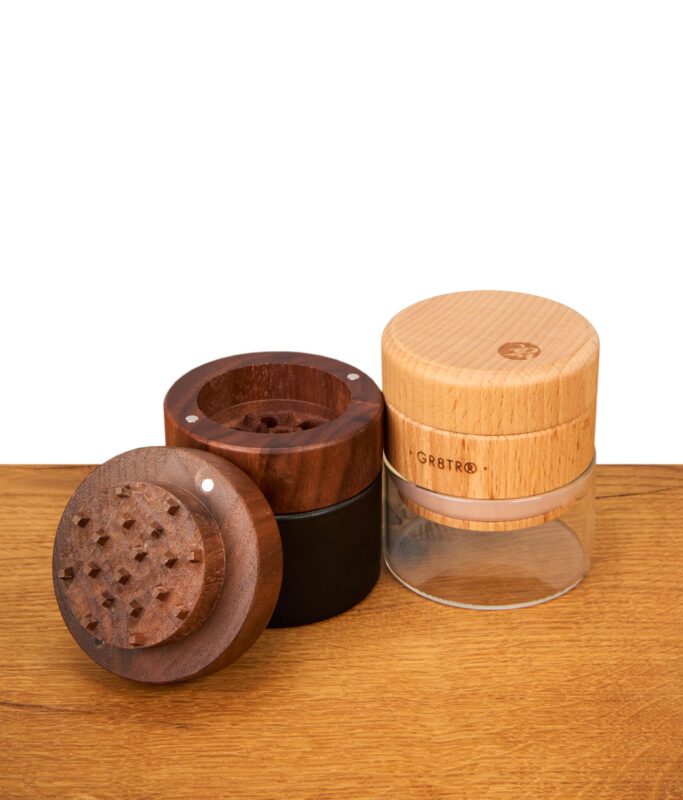 Geöffnete RYOT GR8TR Holz-Grinder in Walnuss und hellem Holz mit sichtbarem Mahlwerk, mattschwarzem Unterteil und Glas-Aufbewahrung.