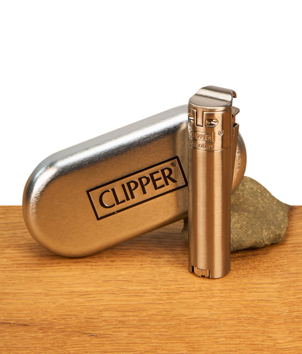 clipper-feuerzeug-metall-jetflame-silber-jpg Gebürstetes Clipper Feuerzeug Metall Jetflame Silber neben einem passenden, geprägten Metalletui auf einem Holztisch.