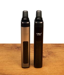 XMax V4 Pro Vaporizer in Silber und Schwarz auf einem Holztisch. Nebeneinander stehende Kräutervaporizer mit Glasmundstück und OLED-Display.