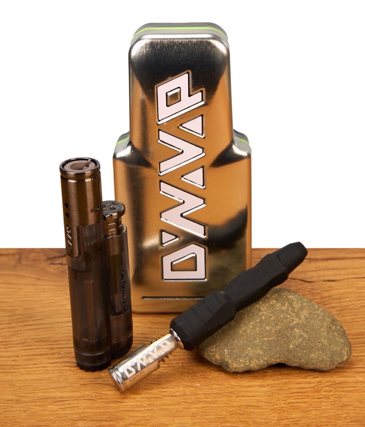 dynavap-the-b2-vaporizer-2-jpg Komplettes DynaVap B2 Vaporizer Set auf Holz: Metall-Case im Hintergrund, Jet-Feuerzeug und auf einem Stein liegender Silikon-Vape.