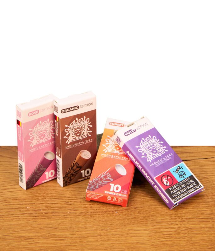 Vier 10er Packungen Medusa Aktivkohlefilter in den Editionen Rosé, Organic, Sunset und Violet auf einem Holztisch.