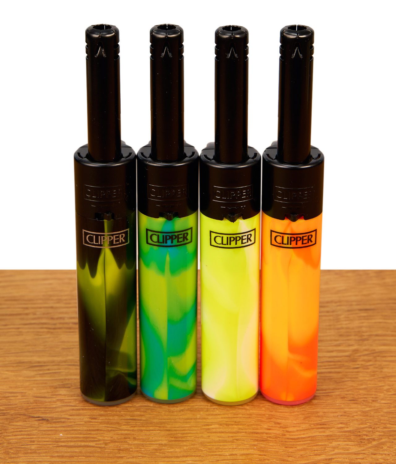clipper-mini-stabfeuerzeug-nebula-mix-4-4er-set-jpg 4er-Set Clipper Mini Stabfeuerzeuge Nebula Mix #4. Verschiedenfarbige, marmorierte Gehäuse mit schwarzen Metallrohren auf Holz.