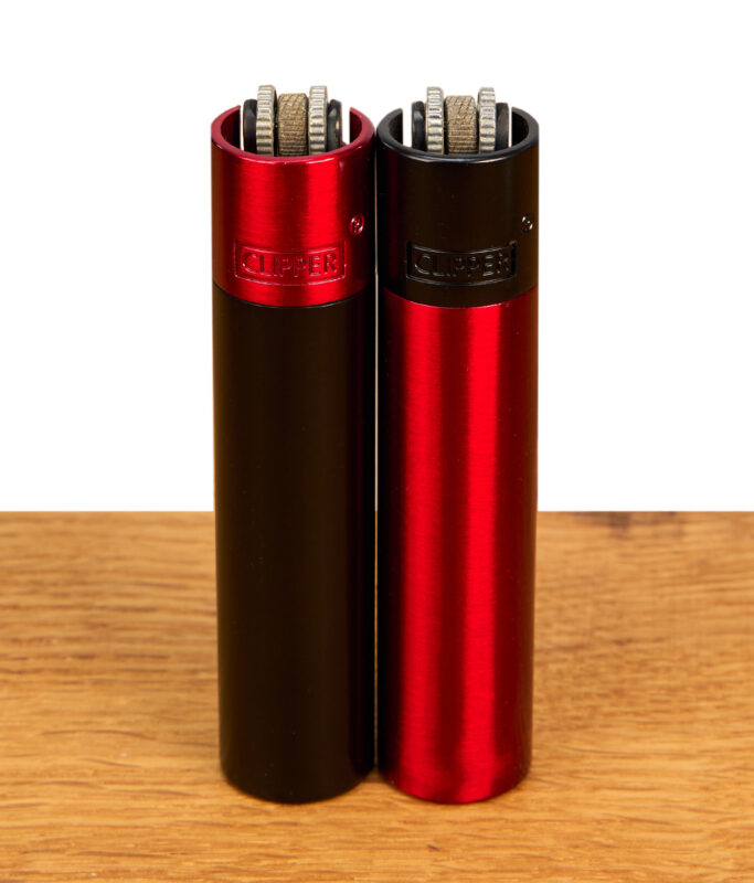 Clipper Metall Lava Feuerzeuge im Duo auf Holz. Gebürstetes Metall in Rot-Schwarz und Schwarz-Rot mit klassischem Zündrad.