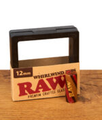 Ein 12mm RAW Whirlwind Glastip mit rot-braunem Spiral-Design und goldenem Logo, stehend neben seiner Display-Verpackung auf Holz.