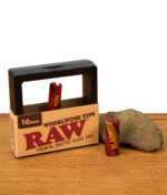 Die 10mm Edition der RAW Whirlwind Tips dekorativ arrangiert mit Verpackung und einem Naturstein auf einer Holzoberfläche auf welcher auch die 12mm Variante steht.