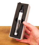 Hand hält den silbernen XMax V4 Pro Vaporizer in der geöffneten weißen Verpackung. Kräutervaporizer mit mattem Finish in schwarzem Schaumstoff.