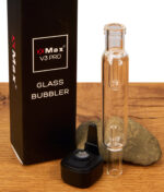 Nahaufnahme des XMax V3 Pro Glass Bubbler. Magnetischer Vaporizer-Sockel mit Edelstahlsieb, Glasaufsatz und Verpackung auf Holztisch.