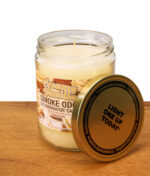 Geöffnete Smoke Odor Duftkerze Creamy Vanilla im großen Glas; der goldene Metalldeckel mit dem bekannten Aufdruck „LIGHT ONE UP TODAY“ lehnt an der vanillefarbenen Kerze.