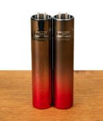 Zwei Clipper Metall Demon Gradient Feuerzeuge im direkten Vergleich nebeneinander auf Holz: Links die hochglänzende (Icy-Optik) und rechts die matte Variante des edlen Metall-Lighters mit rot-schwarzem Farbverlauf.