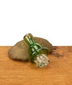 Der grüne Spinner Carb Cap für Quarzbanger aus Borosilikatglas, präsentiert vor einem Stein zur Nutzung bei Dabbing-Session