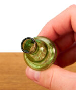Top-down Nahaufnahme des grünen Spinner Carb Caps, der zwischen den Fingern gehalten wird; zeigt die obere Airflow-Öffnung zur präzisen Luftstromkontrolle.