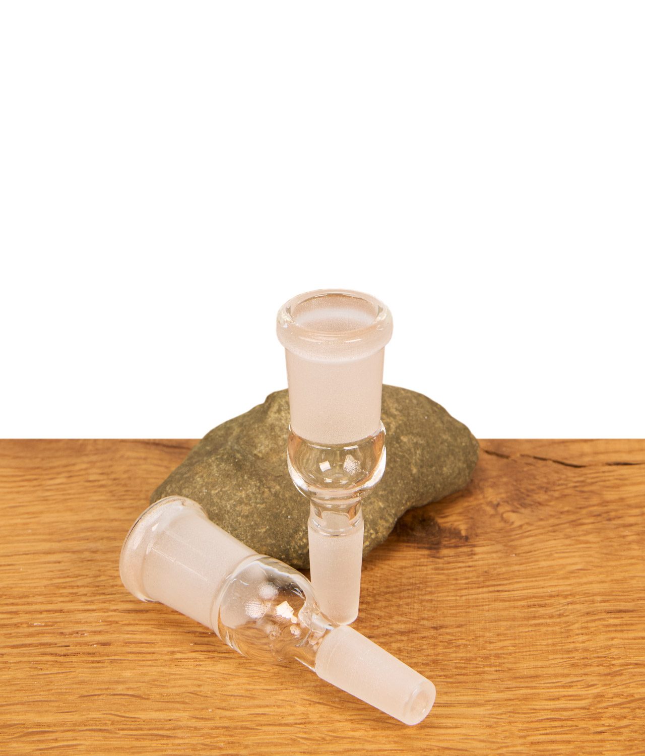 bongadapter-ns10-auf-ns14-erweiterung-1-jpg Zwei gläserne Bongadapter NS10 auf NS14 Erweiterungen auf einer Holzfläche; ein Adapter steht aufrecht vor einem Deko-Naturstein, der andere liegt horizontal davor.