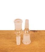Zwei Bongadapter zur Schliff-Erweiterung von NS10 Male auf NS14 Female aus klarem Glas stehen nebeneinander auf Holz, wobei ein Adapter aufrecht und der andere umgedreht platziert ist.