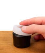 Eine Hand stülpt den elastischen, halbtransparenten Flower Mill Silikon Grip über den Deckel eines schwarzen Grinders, um den Grip beim Mahlen von Kräutern zu optimieren.