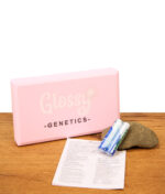 Der vollständige Lieferumfang der Glossy Genetics Digitalwaage 0,01-500g inklusive der geschlossenen rosa Taschenwaage, der Bedienungsanleitung und zwei AAA-Batterien dekorativ auf einem Holztisch arrangiert.