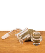Der MJ Arsenal Sidewinder Banger liegt horizontal auf einer Holzoberfläche neben einem massiven Glasstopfen (Carb Cap), der als passender Deckel für die Luftstromkontrolle dient.