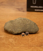 Detailaufnahme der beiden 6mm Terp Pearls des MJ Arsenal Hourglass Banger Sets vor einem Stein auf Holz platziert. Im Hintergrund sieht man die Originalverpackung