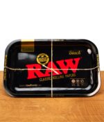 Schwarze RAW Black Classic Rolling Tray Drehunterlage aus Metall mit rotem Logo, mit einer Paketschnur kreuzweise verschnürt.