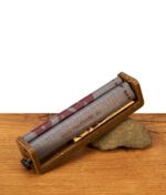 RAW Eco 2-Way Roller Drehmaschine King Size 110mm aus Hanfplastik mit bedrucktem Rollband, gestützt auf einen Stein auf einem Holztisch.