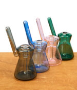 GRAV Hourglass Pocket Bubbler Farbvergleich von schräg hinten – vier kompakte Glas-Rigs auf Holzuntergrund