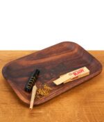 RAW Wooden Rolling Tray Mixing Tray aus Holz im Einsatz. Auf der gemaserten Drehunterlage liegen ein Feuerzeug, Kräuter, ein Joint und RAW-Filtertips.