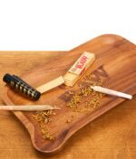 RAW Rolling Tray aus Holz im Einsatz. Auf der gemaserten Drehunterlage liegen lose Kräuter, zwei Joints, ein Feuerzeug und RAW-Filtertips.