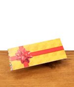 Gelbes Juicy Jay's Happy Birthday Paper Heftchen auf Holz. Geschlossene Verpackung mit aufgedruckter roter Geschenkschleife.
