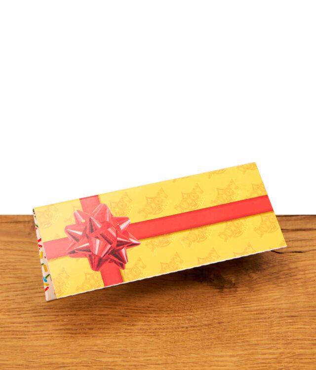 Gelbes Juicy Jay's Happy Birthday Paper Heftchen auf Holz. Geschlossene Verpackung mit aufgedruckter roter Geschenkschleife.