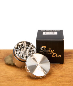 Geöffneter 53mm Steely Dan 2.0 Edelstahl Grinder neben der schwarzen Black Leaf Originalverpackung auf einem Holztisch.