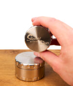 Hand hebt den gefrästen Deckel des Steely Dan 2.0 Edelstahl Grinders an, zeigt das gebürstete Finish auf einem Holztisch.