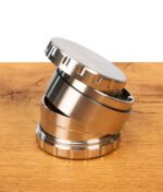 Vierteiliger Steely Dan 2.0 Edelstahl Grinder, dekorativ zerlegt und schräg aufeinander gestapelt auf einem Holztisch.