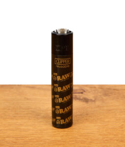 Schwarzes Clipper Feuerzeug RAW Black Edition mit goldenem Logo-Muster, aufrecht auf einem Holztisch.