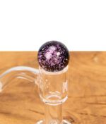 Lilafarbene Glas-Marble aus dem MJ Arsenal Blender Marble Kit auf einem transparenten Quartz Banger platziert, auf einem Holztisch.