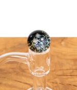 Große Galaxy Glas-Marble des MJ Arsenal Blender Marble Kits, passgenau auf einem Quartz Banger platziert, auf einem Holztisch.