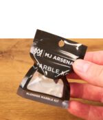 Hand hält die schwarze Originalverpackung des MJ Arsenal Blender Marble Kits mit Sichtfenster über einem Holztisch.