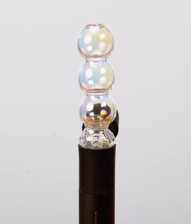 Schimmernder Puffco Pivot Bubble Top Iridescent aus Glas. Der kugelförmige Aufsatz ist passgenau auf den schwarzen Vaporizer aufgesteckt.