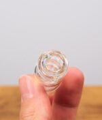 Gläserner Big Fun Pivot Top in der Hand gehalten. Die Nahaufnahme zeigt das obere Zugloch und die schillernde Oberfläche des Glasaufsatzes.