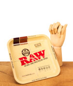 Quadratisches RAW Square Rolling Tray Classic aus Metall. Die hellbraune Drehunterlage steht neben einer Holzhand auf einem Tisch.