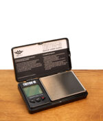 Geöffnete MyWeigh Triton-M digitale Taschenwaage mit Edelstahl-Wiegefläche und Schutzdeckel auf Holzfläche.