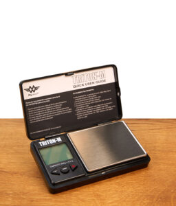Geöffnete MyWeigh Triton-M digitale Taschenwaage mit Edelstahl-Wiegefläche und Schutzdeckel auf Holzfläche.