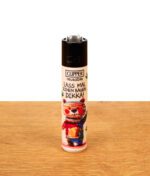 Wiederbefüllbares Clipper FFX 420 Kritzel #2 Feuerzeug mit Bären-Motiv und Text „Lass mal einen bauen, dikka!“ auf Holz.