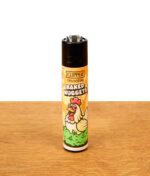 Nachfüllbares Clipper Stoned Animals #3 Feuerzeug mit Hühner-Motiv und dem Schriftzug „Baked Nuggets“ auf einer Holzoberfläche.