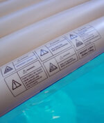 Aufgedruckte Sicherheitswarnungen auf dem robusten Vinyl-Material der RAW Floaty Pack Luftmatratze im Wasser.