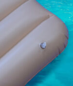 Nahaufnahme des transparenten Ventils der beigefarbenen RAW Floaty Pack Luftmatratze auf klarem Poolwasser.