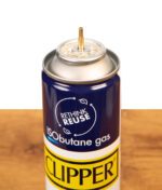 Detailansicht der messingfarbenen Fülldüse und des blauen Rethink-Reuse Logos der Clipper Feuerzeuggas 300ml Dose auf Holz.